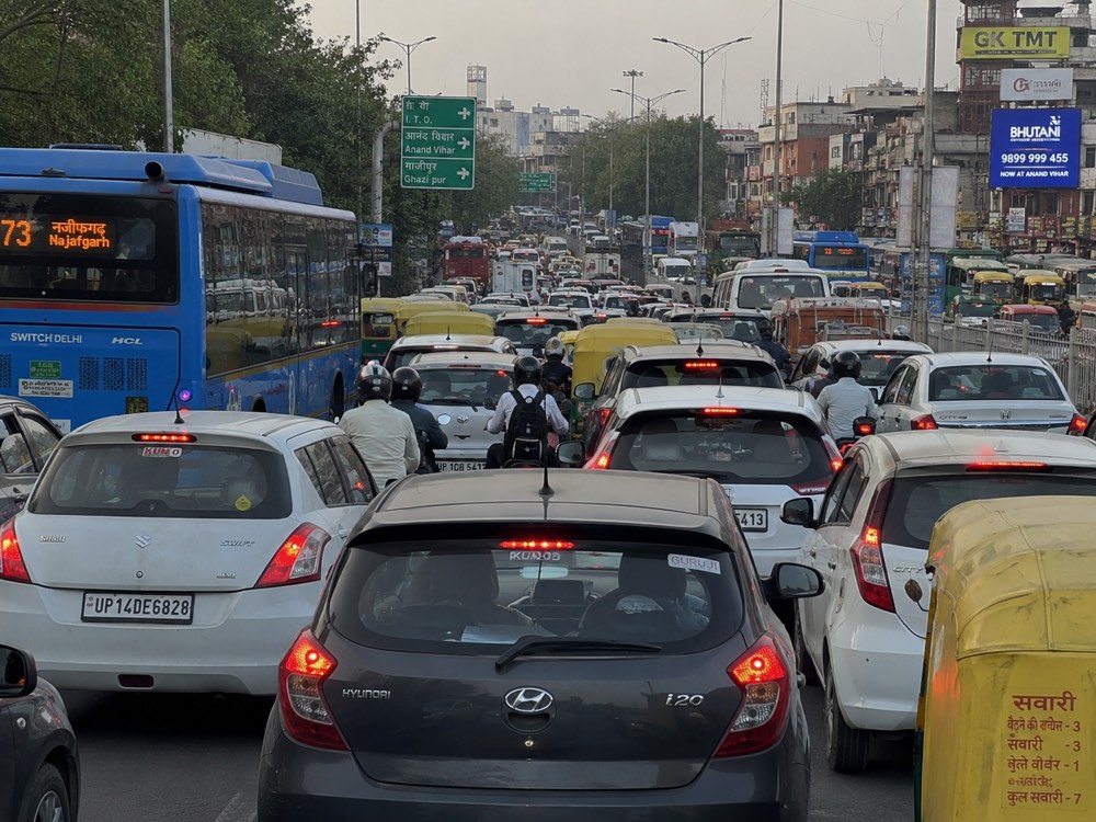 Gridlocked Indian arterial road — cars, two-wheelers, autos and a city bus packed bumper-to-bumper at a choke point